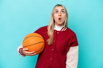 Wall Mural - Young caucasian basketball player woman isolated on blue background looking up and with surprised expression