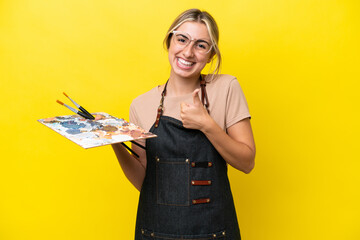 Wall Mural - Young artist caucasian woman holding a palette isolated  on yellow background giving a thumbs up gesture