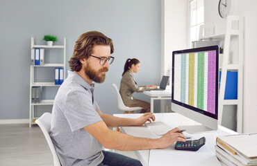 Wall Mural - Male accountant uses calculator to calculate financial report working at office with computer. Man working with financial software sitting at desk on colleague background. Finances and economy concept