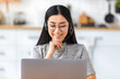 © kucherav - Portrait of a smiling woman in headset, looking at laptop screen, having video call discussing something, female freelancer working remotely online at home