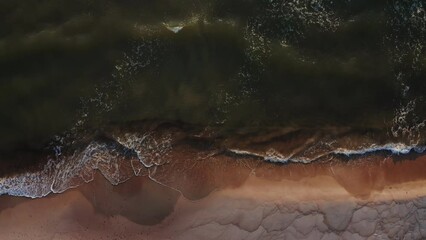 Wall Mural - Top view from a drone of the coastline at high tide. Foamy sea waves crash against the shore, leaving patterns on the sand. Bird's-eye view.