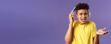 What Do You Want, I Am In Headphones. Portrait Of Confused Annoyed Young Man Shrugging, Take-off Earphone To Hear What Person Asked While He Was Listening Music, Purple Background