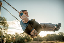 Cute Mixed Race Three Year Old Boy Playing On A Swing In A Suburban Playground