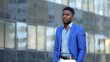 © lenblr - African American man wearing blue blazer and shirt walks past office building. Mature businessman goes to office thinking about startup plan