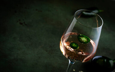 Wall Mural - Rose pink wine with jalapeno pepper in wine glass, dark background, copy space