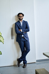 Happy young indian business man ceo leader, arab professional manager, eastern businessman executive wearing suit standing arms crossed looking at camera on white office wall, vertical portrait.