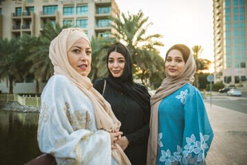 Wall Mural - Arabic women wearing traditional abaya dress meeting and having fun in Dubai - Happy beautiful muslim females bonding outdoors in the city