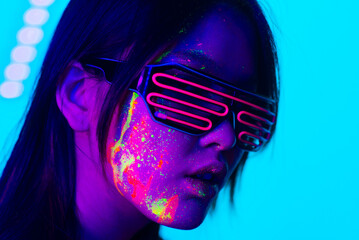 Fashion model with fluo painting on the face - Creative fashion portrait of young beautiful asian woman with fluorescent make-up, futuristic and metaverse concept