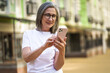 © Svyatoslav Lypynskyy - Mature woman with modern technologies. Senior grey hair lady holding smartphone standing outdoor at the streets of old town. Mature woman read text message standing or walking outdoors