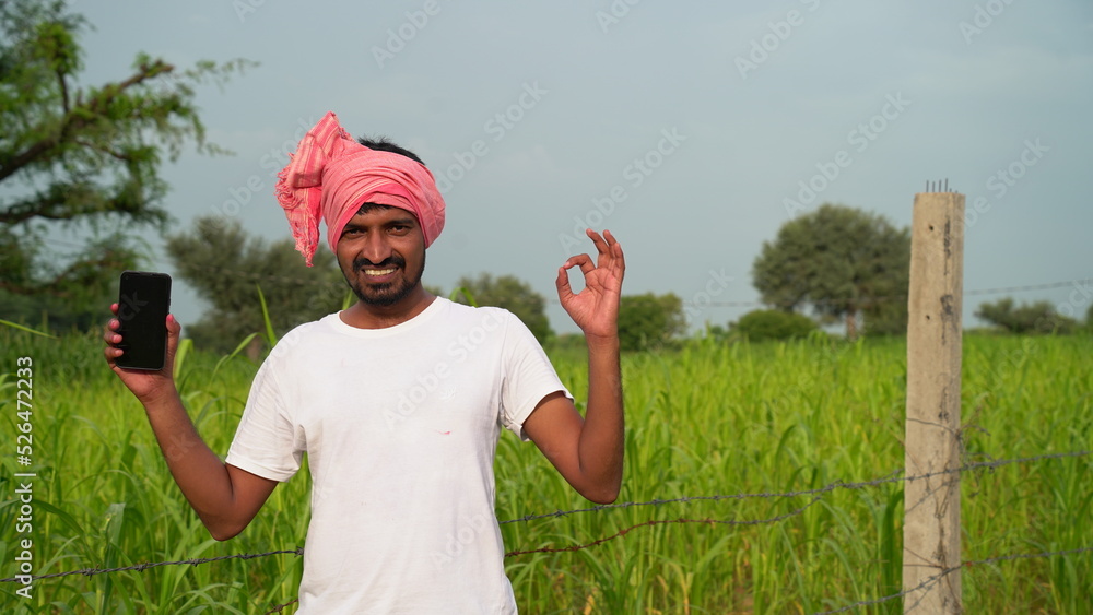 Young indian farmer showing smartphone screen at agriculture field ...
