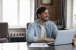 © fizkes - Happy millennial freelance businessman smiling, looking away at home office workplace, sitting at laptop computer and paper document on work table, thinking over successful project future vision
