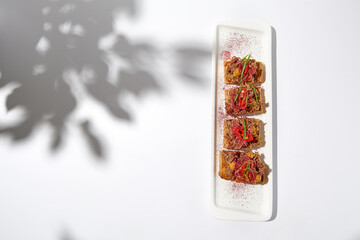 Canvas Print - Aesthetic composition with shredded beef bruschetta on white background with shadows from flowers. Italian bruschetta with shredded beef and mustard on fine dining in summer. Elegant menu concept.