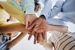 © Seventyfour - Low angle of diverse schoolchildren stacking hands and huddling in team exercise in classroom