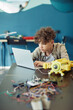 © Seventyfour - Vertical portrait of young curly haired boy using laptop in school during engineering class and programming robot