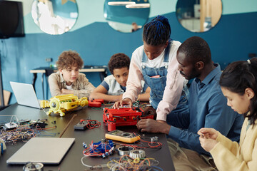 Portrait of black teenage girl building robot with diverse group of children during engineering class in school