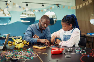 Wall Mural - Portrait of black young girl building robots with male teacher helping during engineering class at school