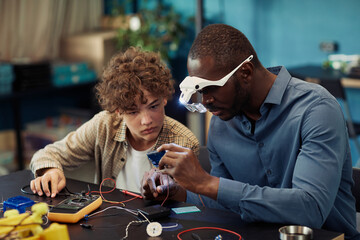 Wall Mural - Portrait of young teenage boy building robots in engineering class with male teacher helping