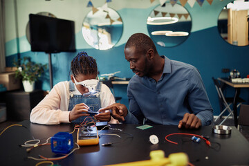 Wall Mural - Portrait of black teen girl building robot in engineering class with male teacher helping