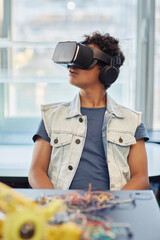 Wall Mural - Vertical portrait of black teenage boy using VR technology in engineering class and looking around