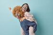 © wayhome.studio  - Positive young women friends have fun together give piggyback ride wear slumber suits apply beauty mud mask undergo skin care procedures isolated against blue background. Friendship concept.