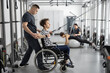 Rehabilitation specialist helps a guy in a wheelchair to do exercise on decompression simulator for recovery from injury. Concept of physical therapy for people with disabilities