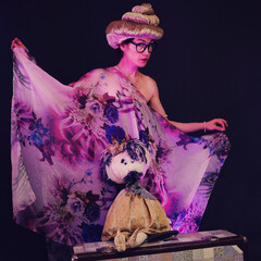 Wall Mural - Happy woman in funny wigs give a performance on a studio black background. Smiling woman showing a humorous show on a dark background