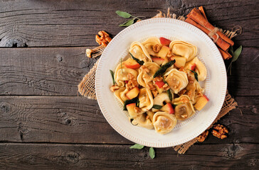 Poster - Autumn pumpkin and apple tortellini pasta with walnuts and brown butter sage sauce. Above view with frame of ingredients on a dark wood background.