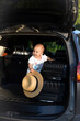 Car trip with a child. Open trunk of the car. Suitcases on the road. Baby with a traveler's hat