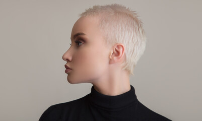 Portrait of a beautiful blonde girl with a short haircut. Side view. Grey background.