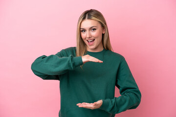 Young caucasian woman isolated on pink background holding copyspace imaginary on the palm to insert an ad