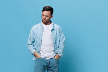 Wall Mural - Pensive upset thoughtful tanned handsome man in casual basic t-shirt hold hands on jeans pocket posing isolated on blue studio background. Copy space Banner Mockup. People emotions Lifestyle concept