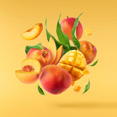 Wall Mural - Fresh ripe whole and sliced mango and peaches with green leaves falling in the