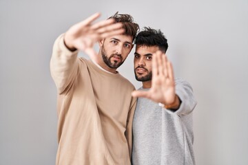 Wall Mural - Young homosexual couple standing over white background doing frame using hands palms and fingers, camera perspective