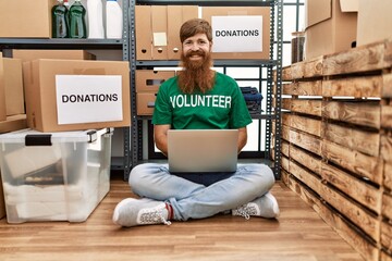 Poster - Caucasian man with long beard wearing volunteer t shirt using laptop looking positive and happy standing and smiling with a confident smile showing teeth