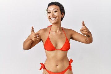 Canvas Print - Young hispanic woman with short hair wearing bikini success sign doing positive gesture with hand, thumbs up smiling and happy. cheerful expression and winner gesture.