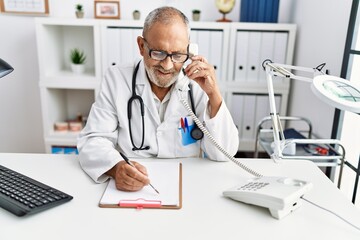  Senior grey-haired man wearing doctor uniform talking on the telephone at clinic