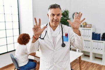 Canvas Print - Middle age doctor man at the clinic with a patient showing and pointing up with fingers number eight while smiling confident and happy.