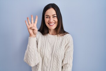 Sticker - Young brunette woman standing over blue background showing and pointing up with fingers number four while smiling confident and happy.