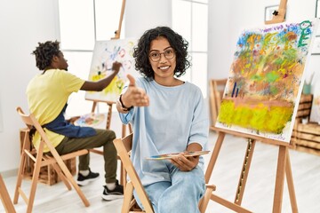 Sticker - Young hispanic woman at art studio smiling cheerful offering palm hand giving assistance and acceptance.