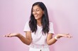 © Krakenimages.com - Young hispanic woman standing over pink background smiling showing both hands open palms, presenting and advertising comparison and balance