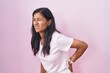 © Krakenimages.com - Young hispanic woman standing over pink background suffering of backache, touching back with hand, muscular pain