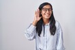 © Krakenimages.com - Young hispanic woman wearing glasses smiling with hand over ear listening an hearing to rumor or gossip. deafness concept.