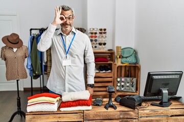 Sticker - Middle age hispanic man working as manager at retail boutique doing ok gesture with hand smiling, eye looking through fingers with happy face.