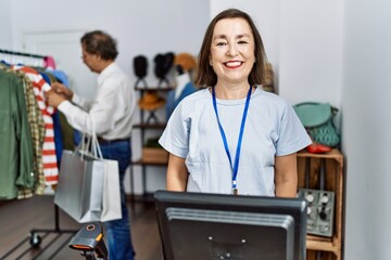 Wall Mural - Middle age hispanic woman working as manager at retail boutique looking positive and happy standing and smiling with a confident smile showing teeth