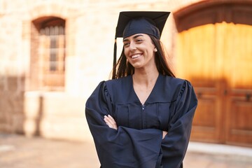 Wall Mural - Young hispanic woman wearing graduated uniform standing with arms crossed gesture at university