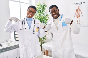 Sticker - Young african american doctors working at medical clinic looking confident with smile on face, pointing oneself with fingers proud and happy.