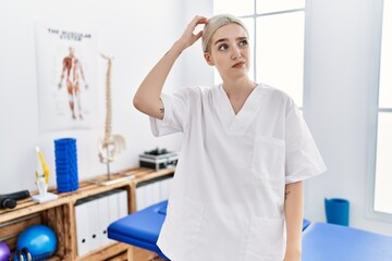 Sticker - Young caucasian woman working at pain recovery clinic confuse and wondering about question. uncertain with doubt, thinking with hand on head. pensive concept.