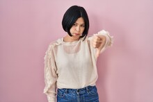 Young Asian Woman Standing Over Pink Background Looking Unhappy And Angry Showing Rejection And Negative With Thumbs Down Gesture. Bad Expression.