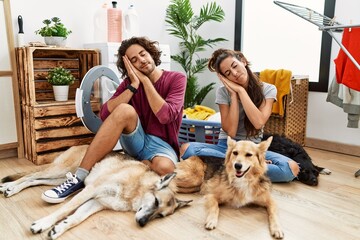 Sticker - Young hispanic couple doing laundry with dogs sleeping tired dreaming and posing with hands together while smiling with closed eyes.