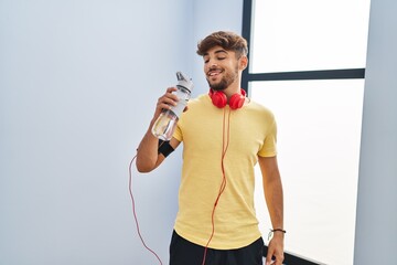 Sticker - Young arab man drinking water wearing headphones at sport center